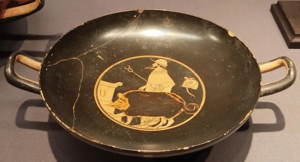 Ancient Greek red-figure kylix with two handles, showing Hermes with a traveler's hat and caduceus, leading a sacrificial pig to an altar. Circa 510–500 BCE.