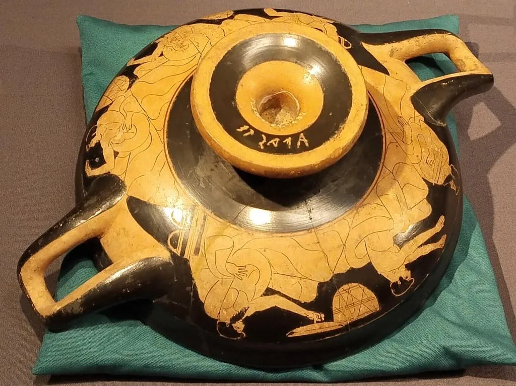 Upside-down ancient Greek red-figure kylix with two handles, showing reclining youths in symposium scenes, ca. 480 BCE.