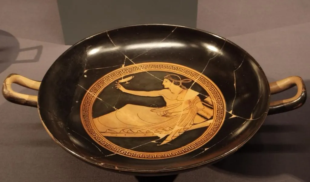 Ancient Attic red-figure kylix with two handles, tondo shows a reclining youth playing kottabos. Dated around 500 BCE.
