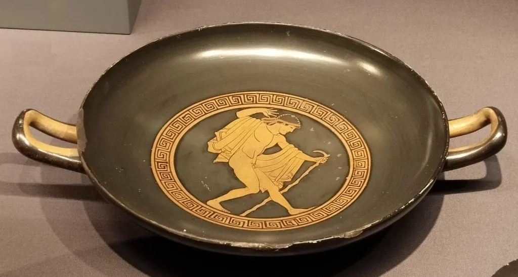 Ancient Greek red-figure kylix with two horizontal handles, depicting a nude youth holding a stick within a meander-framed tondo. Made in Attica, 5th century BCE.