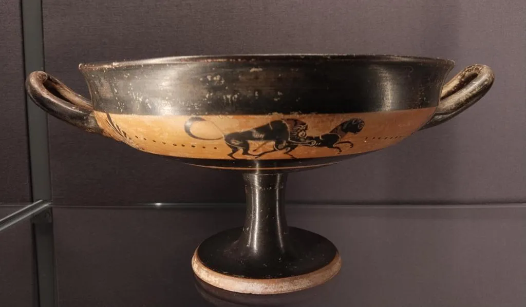 Ancient Greek black-figure kylix on a high stem, decorated with a lion attacking a prey animal in a band across the body. Circa 550 BCE.