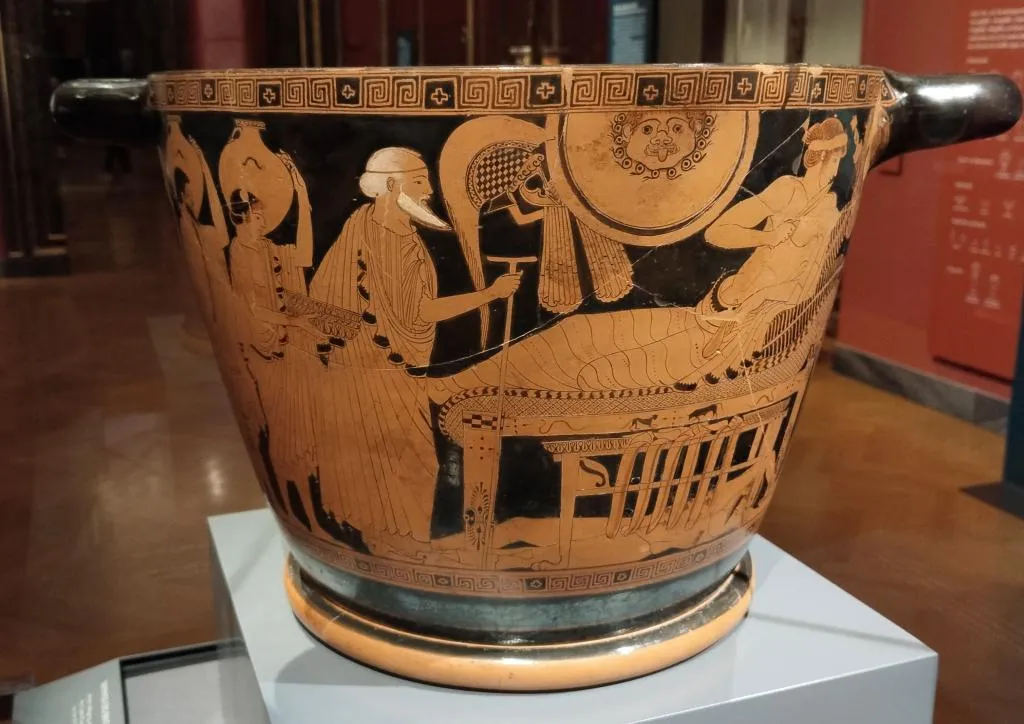 Red-figure Greek skyphos showing an elderly Priam approaching Achilles, who reclines on a couch; Hector’s body lies beneath, and a servant stands with a wine strainer.