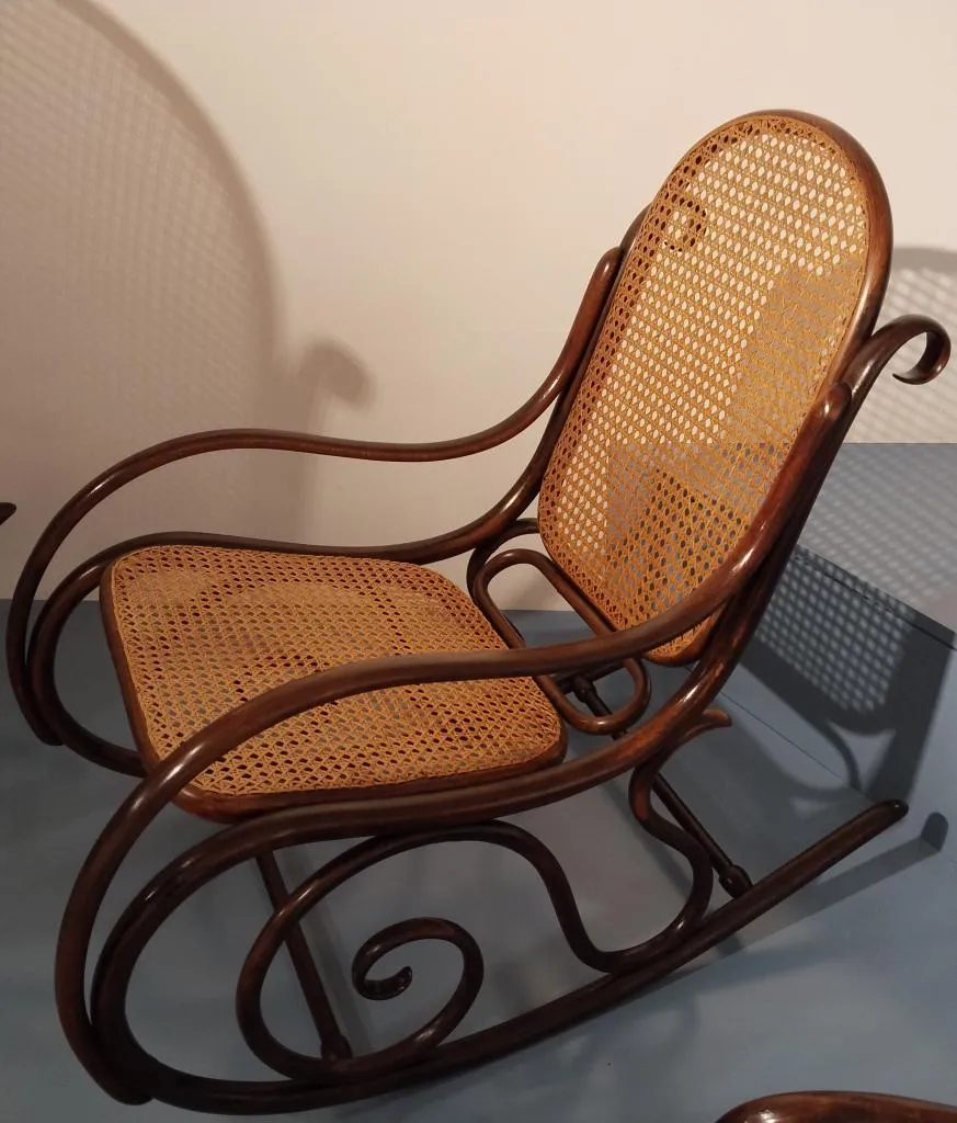 Fotografie eines Thonet-Schaukelstuhls mit geschwungenem Bugholzrahmen, Rückenlehne und Sitz aus Rohrgeflecht, typisch für die Bugholzkunst des Unternehmens.