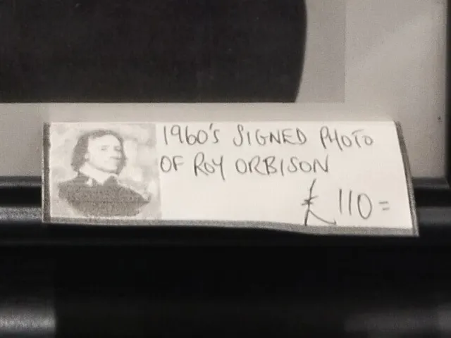 AI-generated image description: This is the price tag in the Cromwell Antique Center for a signed photo of Roy Orbison. The tag reads 1960's Signed Photo of Roy Orbison and lists the price as £110. The tag also features a small black-and-white image of Oliver Cromwell. The handwriting on the tag adds a personal and authentic touch to the display.