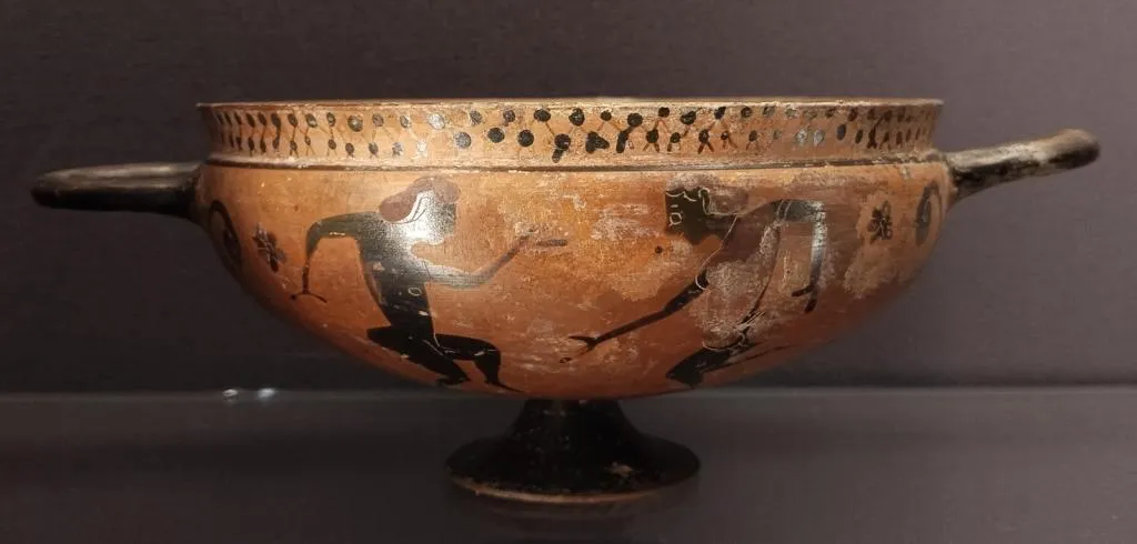 Ancient Greek black-figure kylixwith an offset lip, showing two dancing male youths, decorated around the body with dotted patterns and floral motifs, dated circa 560 BC.