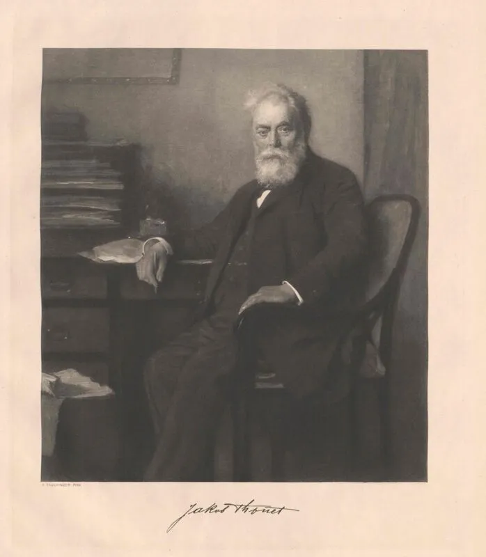 Schwarz-weiß-Porträt von Jakob Thonet, an einem Schreibtisch sitzend, im dunklen Anzug und mit weißem Bart, dargestellt im formellen Stil des 19. Jahrhunderts.