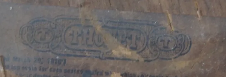 Close-up of a faded later Thonet paper label on a wooden frame, showing THONET in bold black letters with simplified decorative elements.