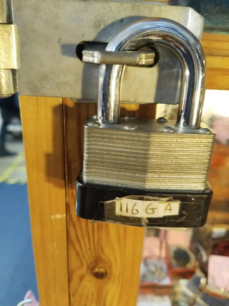 The image features a close-up of a padlock securing a wooden door or cabinet. The padlock has a piece of tape with the handwritten label 116 GA.