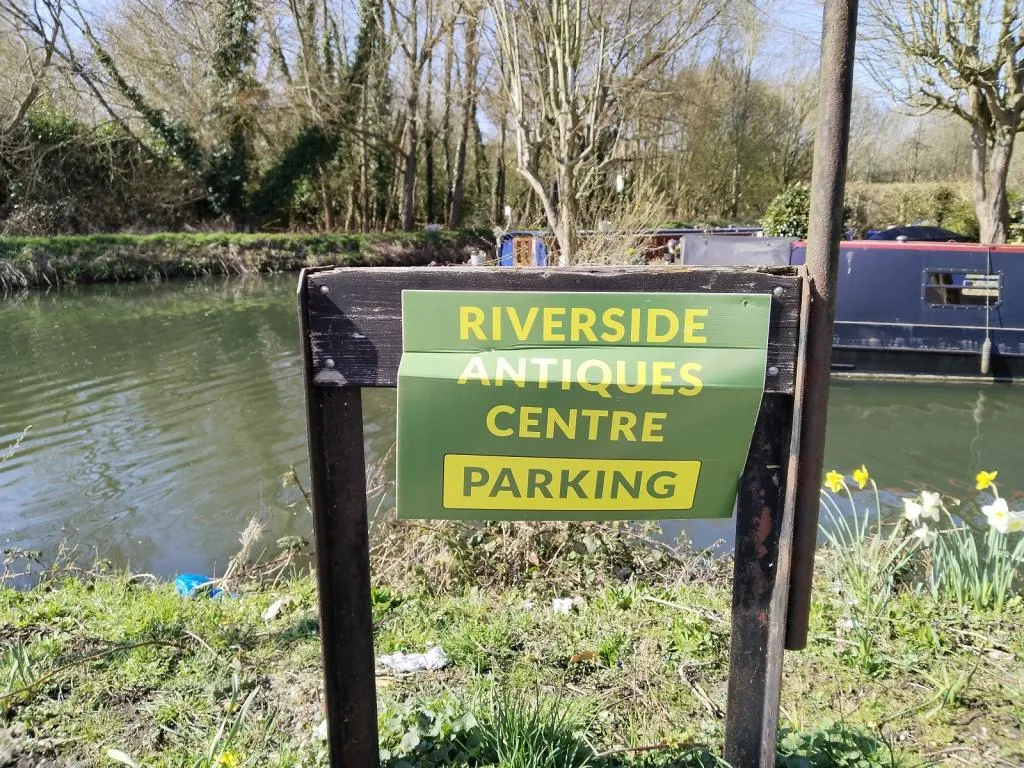 Riverside Antiques Centre parking sign by the river—marking the scenic entrance accessible from the towpath side.