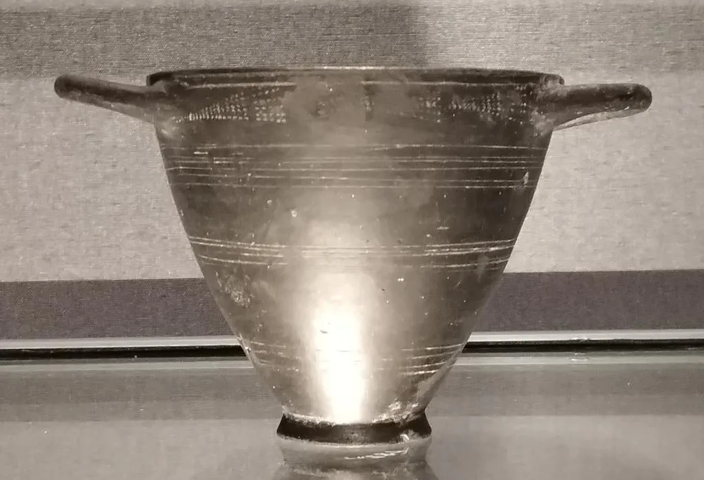 Frühgriechischer Skyphos bzw. Kotyle mit konischem Korpus, waagerechten Henkeln und eingeritzten Linien- und Fächerverzierungen; dunkle Engobe.