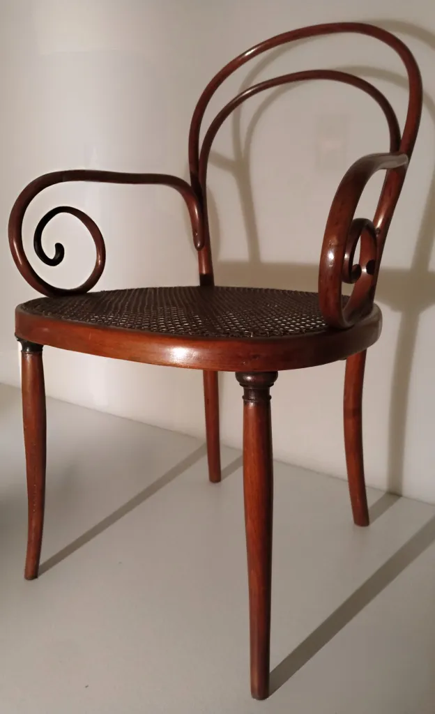 Side view of Thonet bentwood armchair Model No. 8, featuring round cane seat, turned front legs, and spiraled armrests integrated into the double-arched backrest.