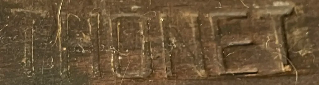 Macro view of a wooden seat frame with the word THONET pressed in block letters, showing wear and age.