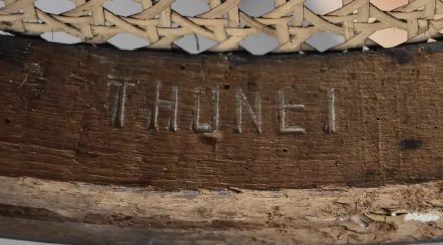 Close-up of an embossed THONET stamp pressed into the wooden seat frame of a bentwood chair with woven cane seat.