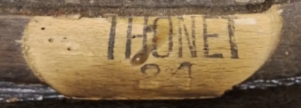 Nahaufnahme eines flachen Tintenstempels mit der Aufschrift THONET und der darunter gesetzten Zahl 24 auf einem hölzernen Stuhlrahmen.
