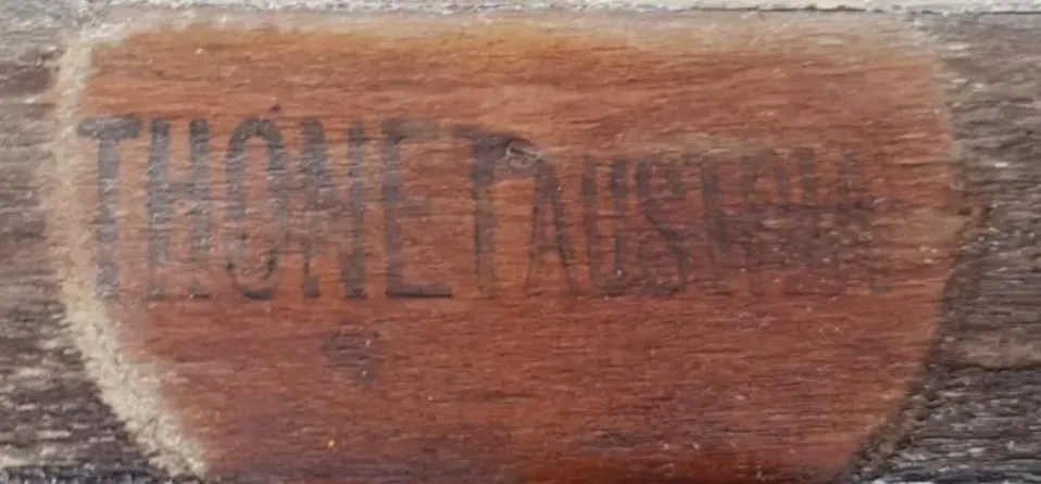 Close-up of a flat black ink stamp reading THONET AUSTRIA on a wooden chair frame, slightly faded with age.