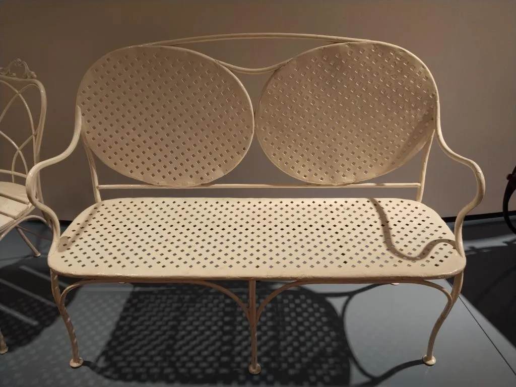 Fotografie eines Thonet Gartenkanapees aus Metall mit zwei ovalen Rückenteilen, durchbrochener Sitzfläche und geschwungenen Armlehnen, später weiß überstrichen.