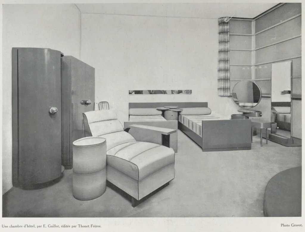 Schwarz-weiß-Fotografie eines Hotelzimmers von 1929, entworfen von E. Guillot und möbliert von Thonet Frères, mit einem Fauteuil, Bett, Kleiderschrank und weiteren modernen Möbeln.