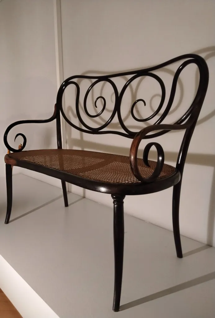 Seitenansicht des Thonet Kanapees Modell Nr. 1 mit Spiralrückenlehne und Sitz aus Rohrgeflecht.