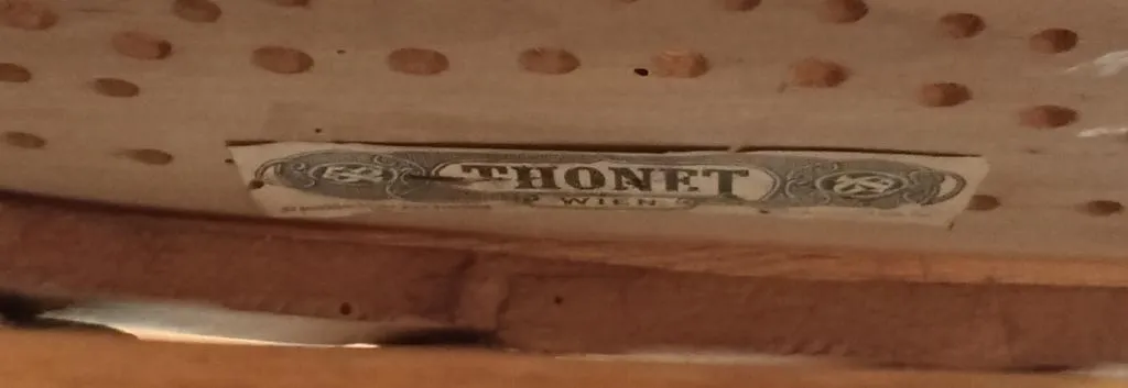 Nahaufnahme eines Thonet-Papieretiketts an der Unterseite einer hölzernen Kinderwiege mit Schaukelgestell, mit der Aufschrift THONET WIEN in kräftigen Buchstaben und dekorativem Rahmen.