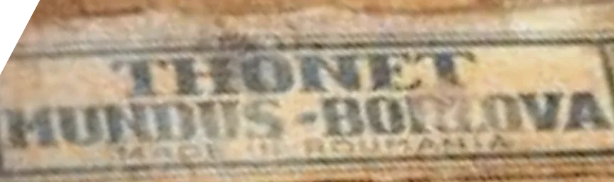 Close-up of a Thonet paper label reading Thonet Mundus – Borlova, Made in Romania, attached to a wooden chair frame, showing the merger-era branding.