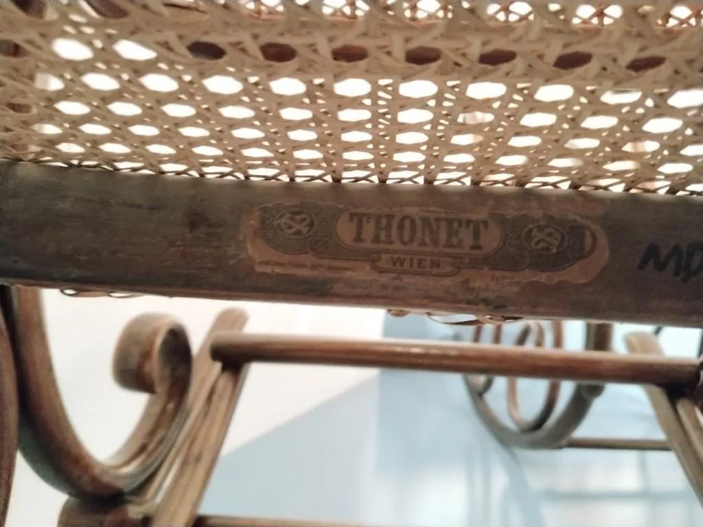 Close-up of a Thonet paper label reading THONET WIEN fixed under the cane seat of a bentwood rocking chair, with curving wood elements visible below.