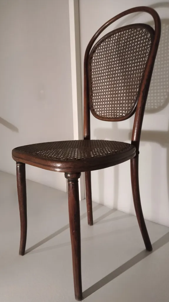 Seitenansicht eines Thonet-Bugholzstuhls Modell Nr. 12 mit ovaler Rückenlehne aus Rohrgeflecht, Rohrsitz und leicht ausgestellten Beinen.