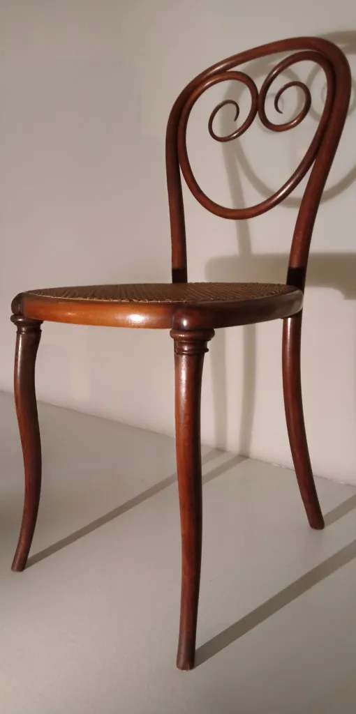 Seitenansicht des Thonet-Stuhls Modell Nr. 2 mit geschwungener Doppelschnecken-Rückenlehne und geflochtener Sitzfläche.