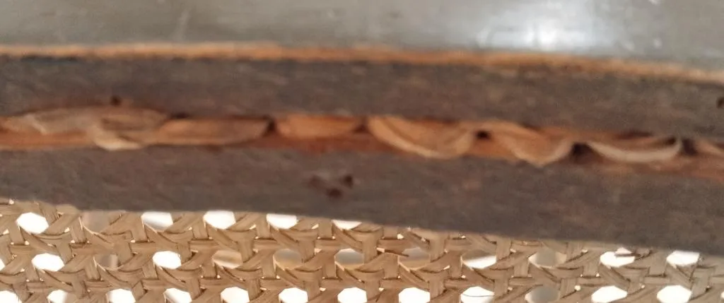 Nahaufnahme von drei kleinen geprägten Punkten in Dreiecksform an der Unterseite eines hölzernen Thonet-Stuhlrahmens unter einer Sitzfläche aus Rohrgeflecht.